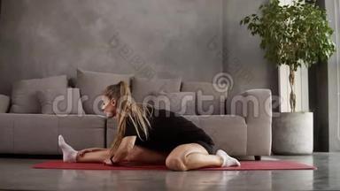 长发，金发，身穿黑色运动服的金发女人在家训练，坐在沙发前的垫子上，伸展肌肉