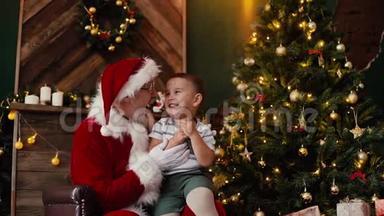 小可爱的男孩许愿坐在圣诞老人的圈里，在圣诞树旁边。