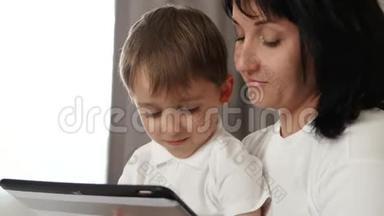 幸福的母亲和儿子的肖像。 母亲在平板电脑上使用一个孩子的发育申请