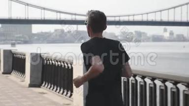 年轻活泼的白种人穿着黑色T恤和短裤沿着<strong>城市</strong>码头奔跑。 <strong>运动</strong>服<strong>运动</strong>员在<strong>城市</strong>跑步。 健康青年