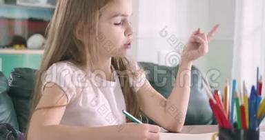 睡觉的白人女孩坐在桌子旁，一只手拿着笔。 筋疲力尽的学童醒来后