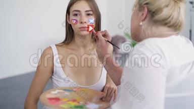 艺术家的肖像画在女孩`脸上使用小软笔和调色板。 身体艺术概念。 艺术作品