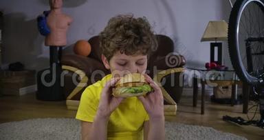 白人男孩在电视前咬汉堡包的特写镜头。 十几岁的卷发小孩在家看电影