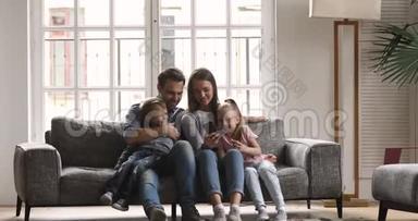 幸福的四口之家用智能手机在沙发上放松