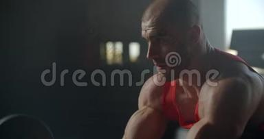 力量训练臂肱二头肌配杠铃.. 身材苗条、肌肉发达的男人举起一个杠铃，坐在健身房里