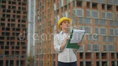 一个戴着安全帽的建筑工地上的女工程师手里拿着一块写字板，一个纸托，上面有一个