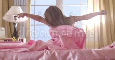 白人女孩早上在粉<strong>红色</strong>的床上醒来。 <strong>儿童</strong>的后视图，长发伸展在阳光下。 童年