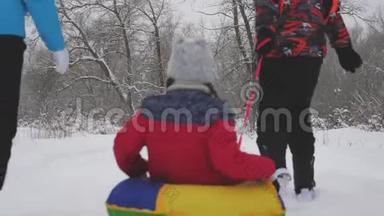 爸爸妈妈和一个孩子在冬天的森林里雪橇。 父母在圣诞公园里扮演一个小女儿。 家庭游戏