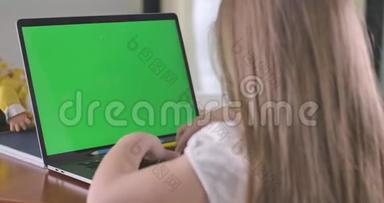 在带有绿色屏幕的笔记本电脑上近距离观看白人学童打字。 在网上学习或利用社交