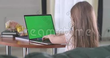 女生在笔记本<strong>电脑</strong>上用绿色屏幕打字的<strong>背面</strong>视图。 在网上学习或使用社交媒体的高加索儿童