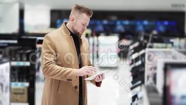 穿棕色外套的年轻帅哥在化妆品店里用数码平板电脑