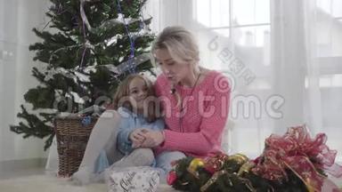 在<strong>圣诞树</strong>的背景下<strong>和</strong>成年女人坐在一起的白人<strong>女孩</strong>微笑。 妈妈<strong>和</strong>她的孩子说话