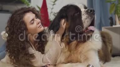 一只大狗和他的女主人躺在家里。 美丽的女人抚摸她的宠物，看着相机和