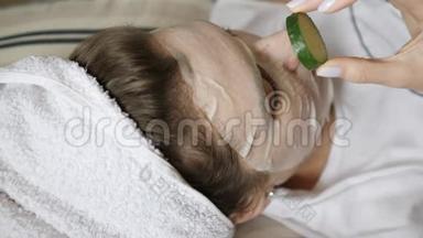 一个穿毛巾的年轻女人把圆圆的黄瓜放在眼睛上。 有机美容护理