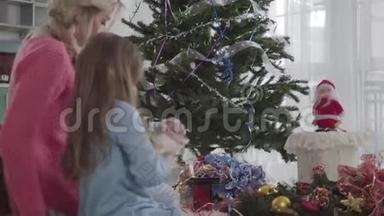 白种人的母亲<strong>和</strong>女儿，选择坐在<strong>圣诞树</strong>旁边的花环。 漂亮的女人<strong>和</strong>漂亮的<strong>女孩</strong>