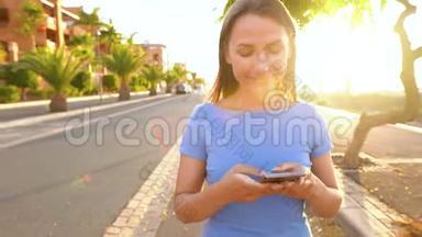 日落时分，一个穿着智能手机的蓝色裙子的女人在棕榈街散步