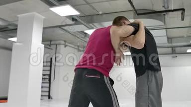 两名摔跤手动作缓慢. 希腊罗马摔跤手穿着T恤衫和外套在大厅里训练。