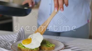 女人把<strong>煎鸡蛋</strong>和鳄梨吐司放在盘子里。 健康素食<strong>早餐</strong>。