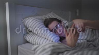戴眼镜的女人躺在床上使用智能手机。 她在这个过程中睡着了，因为她<strong>很累</strong>