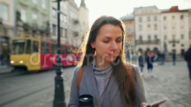 女人手里拿着一个保温杯，在夕阳下用智能手机沿着一条老街走着。 通信、社交网络
