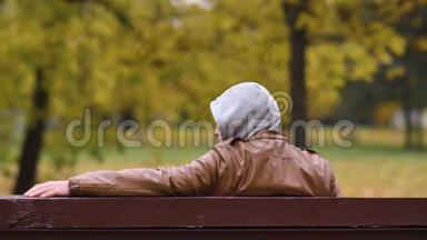 一个不知名的危险人物坐在一个秋天的公园里，坐在长凳上看着，copspace