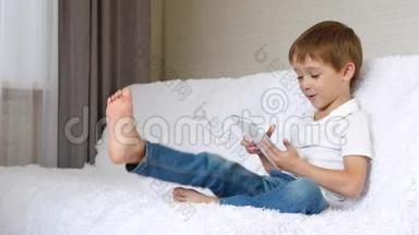 男孩坐在床上，用平板电脑在网上玩或看电影。 孩子感<strong>受到</strong>了
