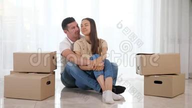 穿牛仔裤的男人女人坐在新房子的光地板上拥抱