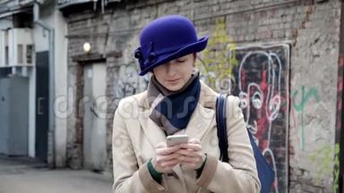 戴着蓝帽子的漂亮女孩近距离在4K街上微笑着看留言电话。
