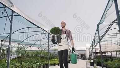 年轻的园丁去温室，手里拿着一个绿色的罐子和漏斗。 稳定摄像机运动，整体