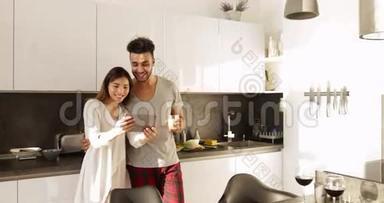 年轻混合种族夫妇使用平板电脑晨曦，快乐西班牙男人亚洲女人一起在厨房