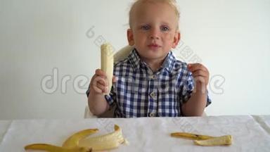 <strong>天真</strong>无邪的孩子吃香蕉坐在桌子旁边白底。万向节运动