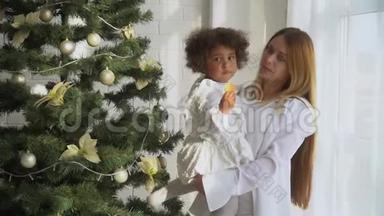 快乐的母亲和穿着白色衣服的小女儿坐在圣诞树旁<strong>吃饼干</strong>