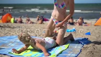 嬉戏的妈妈在沙滩上为她的小女儿做按摩