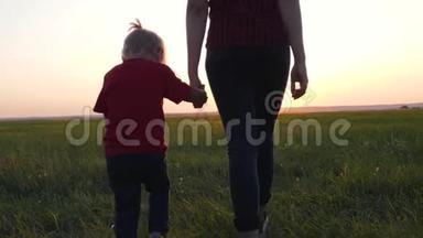一位年轻的母亲牵着女儿`手。 幸福的一家人在夕阳下的清新空气中散步。