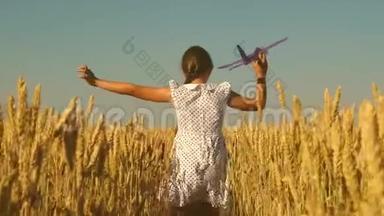 快乐的女孩带着玩具飞机在蓝天下的麦田里奔跑。 孩子们玩玩具飞机。 少年梦想