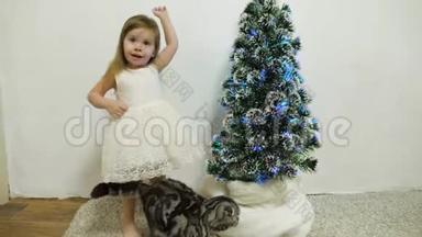 小<strong>女孩</strong>抱着一只猫在<strong>圣诞树</strong>旁的房间里玩。 有漂亮花环的儿童和<strong>圣诞树</strong>
