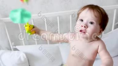 一个穿着尿布的快乐小孩子站在婴儿<strong>床上</strong>，<strong>玩</strong>着<strong>玩</strong>具。 孩子的生活。 婴儿在儿童室<strong>玩</strong>耍