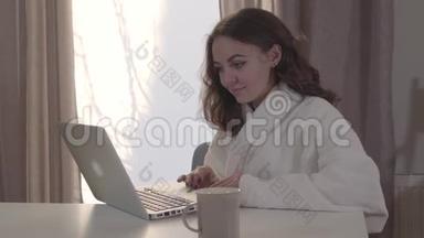 年轻漂亮的白人女孩<strong>在家上网</strong>的肖像。 漂亮的黑发女人用笔记本电脑做脸