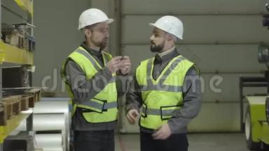 两个白人男子站在仓库里，说话和打手势。 工人在<strong>生产现场</strong>计划时间表。 工厂