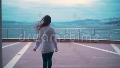 一个女孩正在暴风雨的大海的背景下沿着观景台走着，一个女孩背在镜框里。