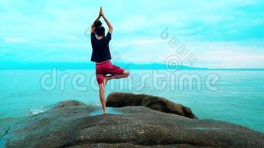 一个男人在海边的大石头上练习瑜伽