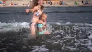 嬉戏的女人和女儿面对海浪。 情绪激动的女孩被泼水
