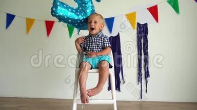 快乐的两岁男孩玩二号气球坐在椅子上。 慢动作