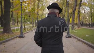 一位白发白种人的背影，他戴着优雅的黑色帽子，穿着外套，在巷子里漫步。成熟的男人