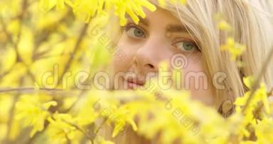 一位年轻迷人的女子，一头金色的<strong>秀发</strong>，在黄色花瓣的花树之间，亲密的肖像。 可爱可爱