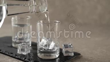 用手将伏特加、龙舌兰酒或清酒从扁平的瓶子中倒入装有冰块的黑色木板上的空杯中