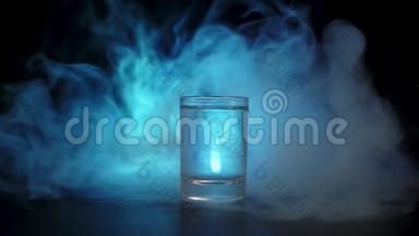 一杯伏特加，龙舌兰酒或清酒放在黑色背景的黑色桌子上。蓝色<strong>烟雾云雾</strong>或蓝色蒸汽