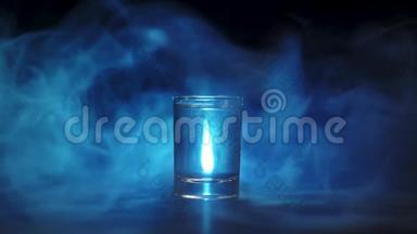 冰块在黑色背景下落入伏特加、龙舌兰酒或清酒的杯中。 蓝色<strong>烟雾</strong>、<strong>云雾</strong>或蓝色蒸汽