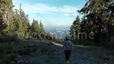 无人机拍摄了一名中年妇女在山林徒步旅行小径上行走，俯瞰一座城市。