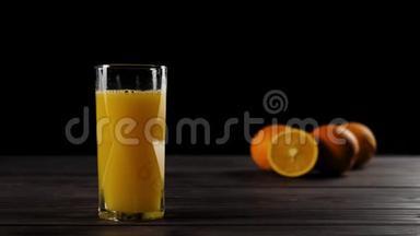 在一个带有新鲜橙汁的仙后座玻璃中掉落的大块冰块在一张木桌上溅起水花和气泡